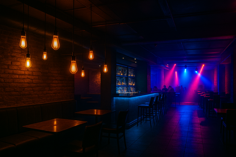 Zoned Nightclub Lighting with LED Edison Bulbs A nightclub interior showing distinct lighting zones: a softly lit lounge area with LED Edison bulbs, a brighter bar area, and dynamic lighting near a dance floor.