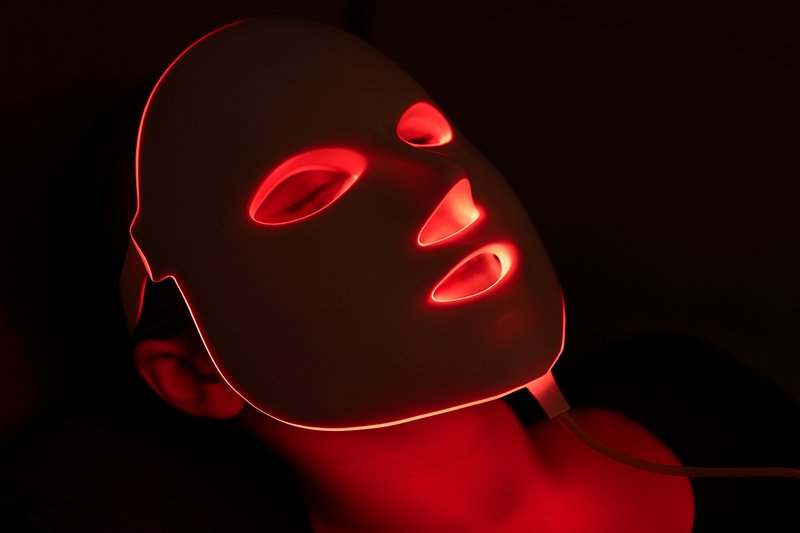 A close-up of a person using a red light therapy LED mask, showing the clean, precise red glow on their skin, conveying a sense of futuristic wellness.