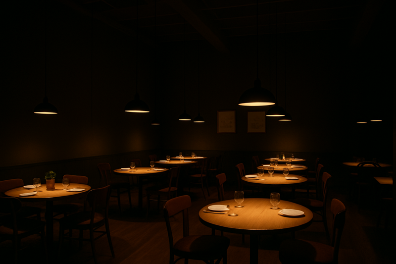A large, high-ceilinged restaurant where the overall ambient light is low, but each table is perfectly illuminated by its own warm, focused spotlight, creating intimate "islands" of light.