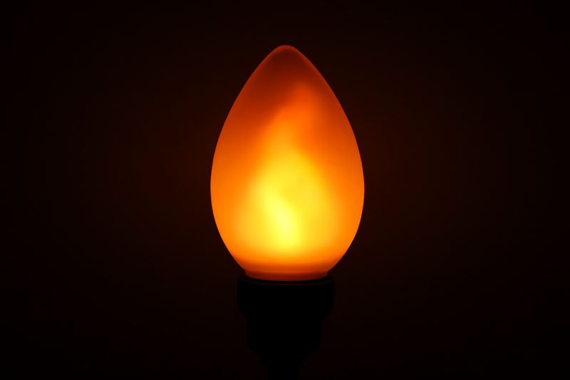 A close-up shot of a high-quality flame-effect bulb in a dark room, showing a convincing, warm, and randomly flickering glow that mimics a real candle