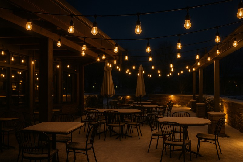 An inviting restaurant patio at night, covered in a light layer of snow, with strings of G45 LED filament bulbs glowing warmly and brightly