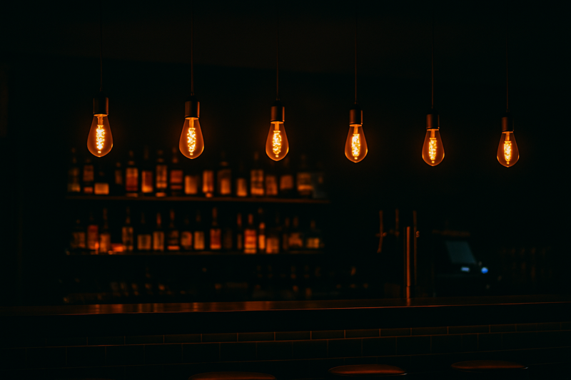 A moody bar scene. A row of pendant lights hangs over the counter. The bulbs are dim and orange, allowing you to see the spiral filament clearly without squinting.