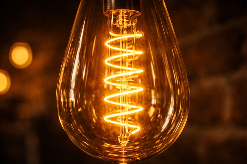 Close up of a Spiral Filament bulb. The glowing yellow coil twists up and down inside the amber glass. It looks vibrant and energetic.