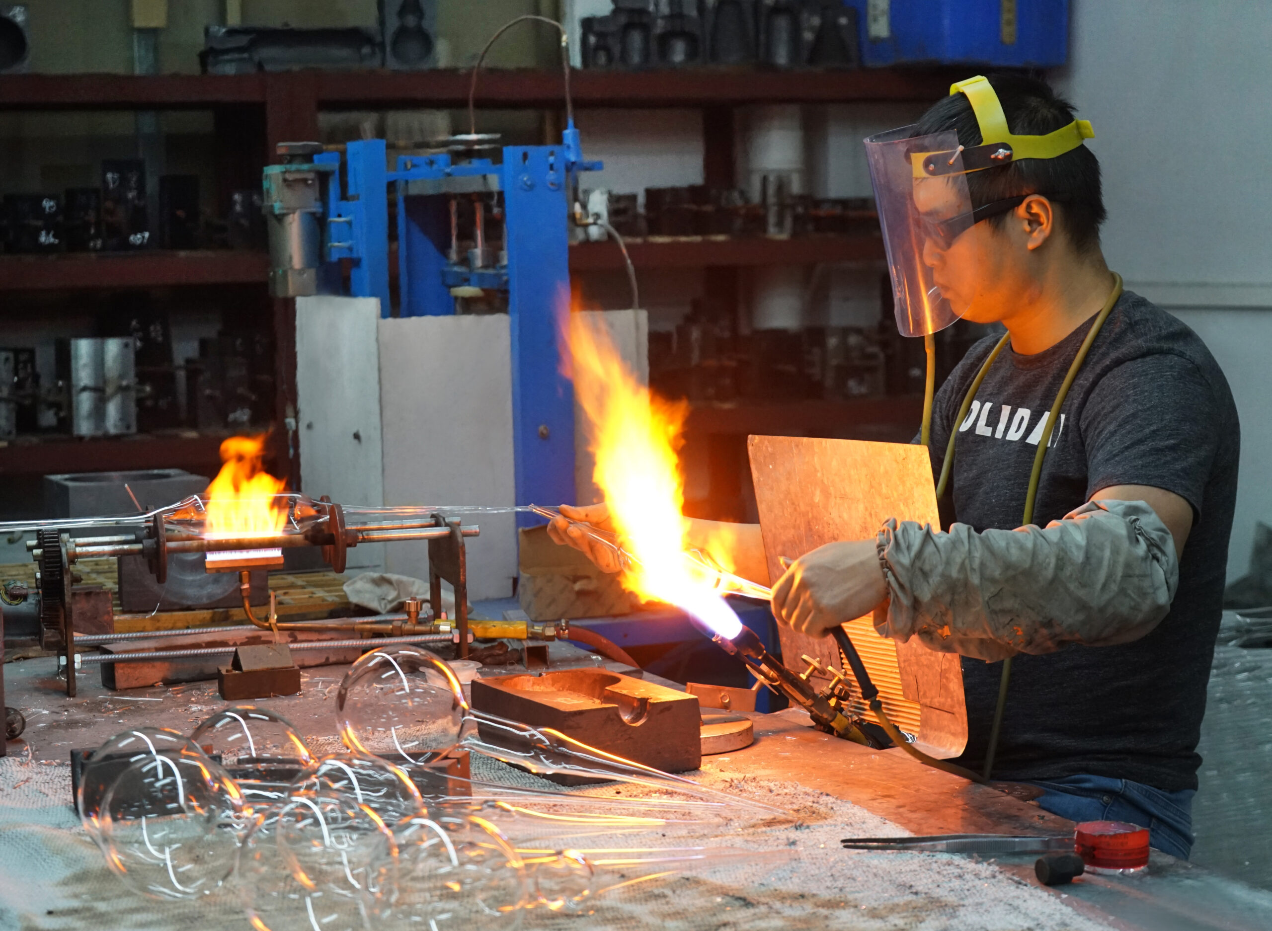 Glass blower hand-crafting a large borosilicate globe bulb in a specialized glass factory