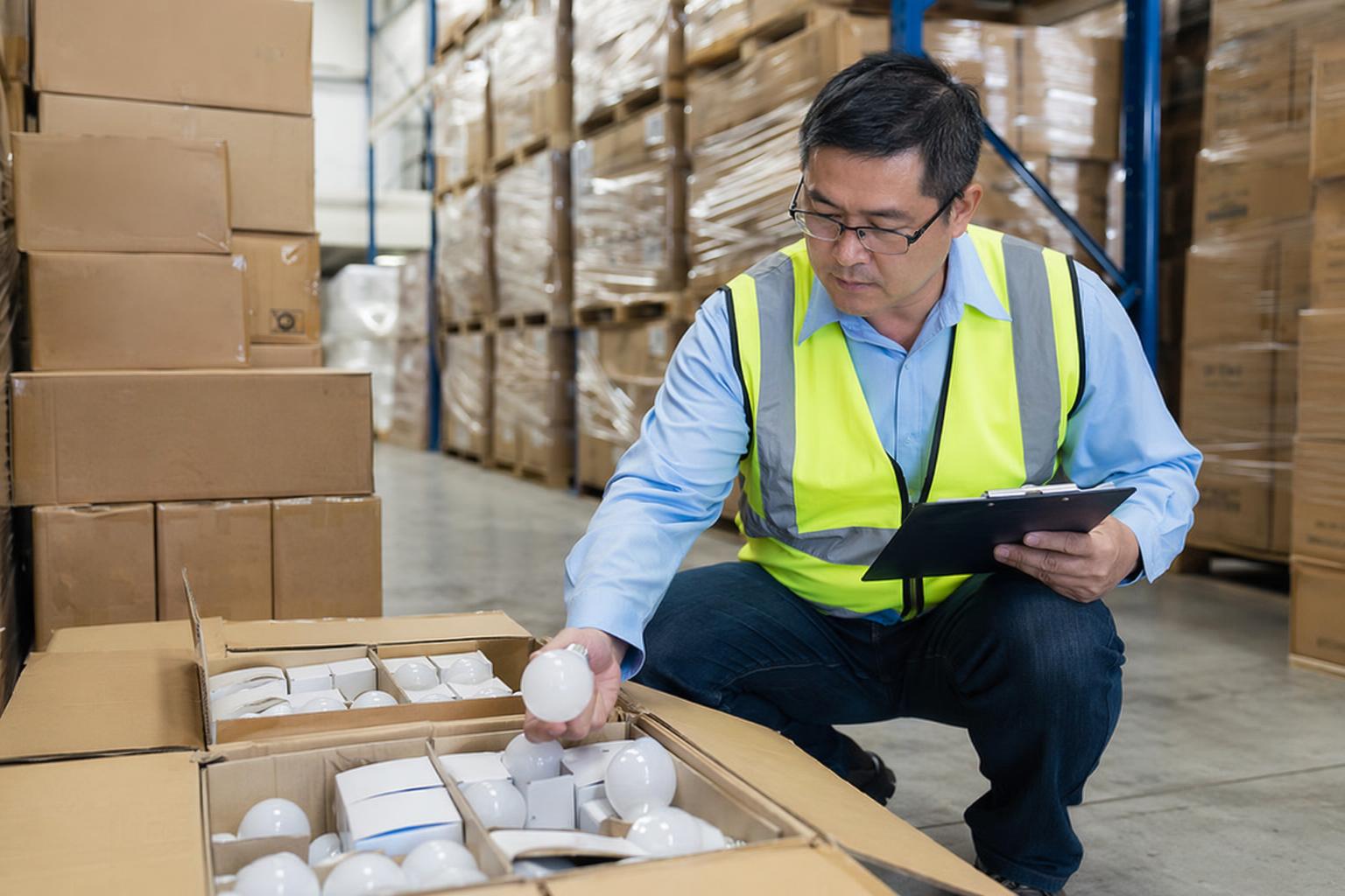 Third party inspector examining LED light bulb shipment at warehouse for quality control before import